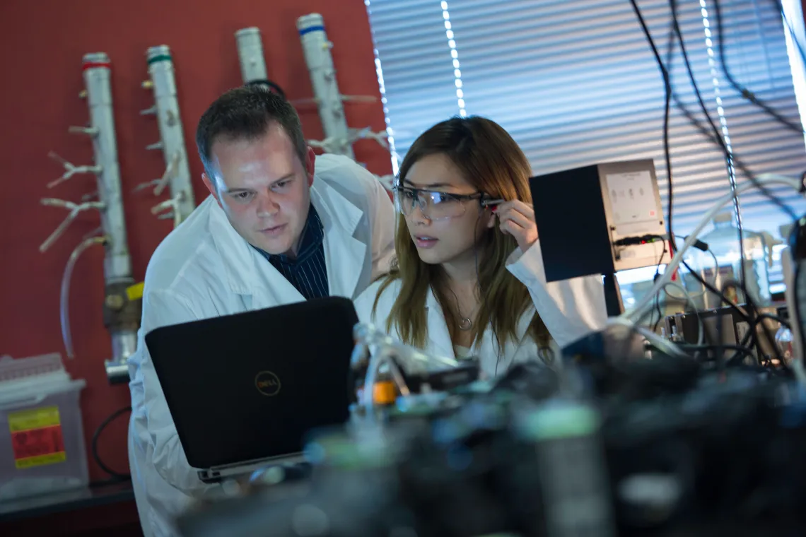 Two students in lab coats looking at a laptop